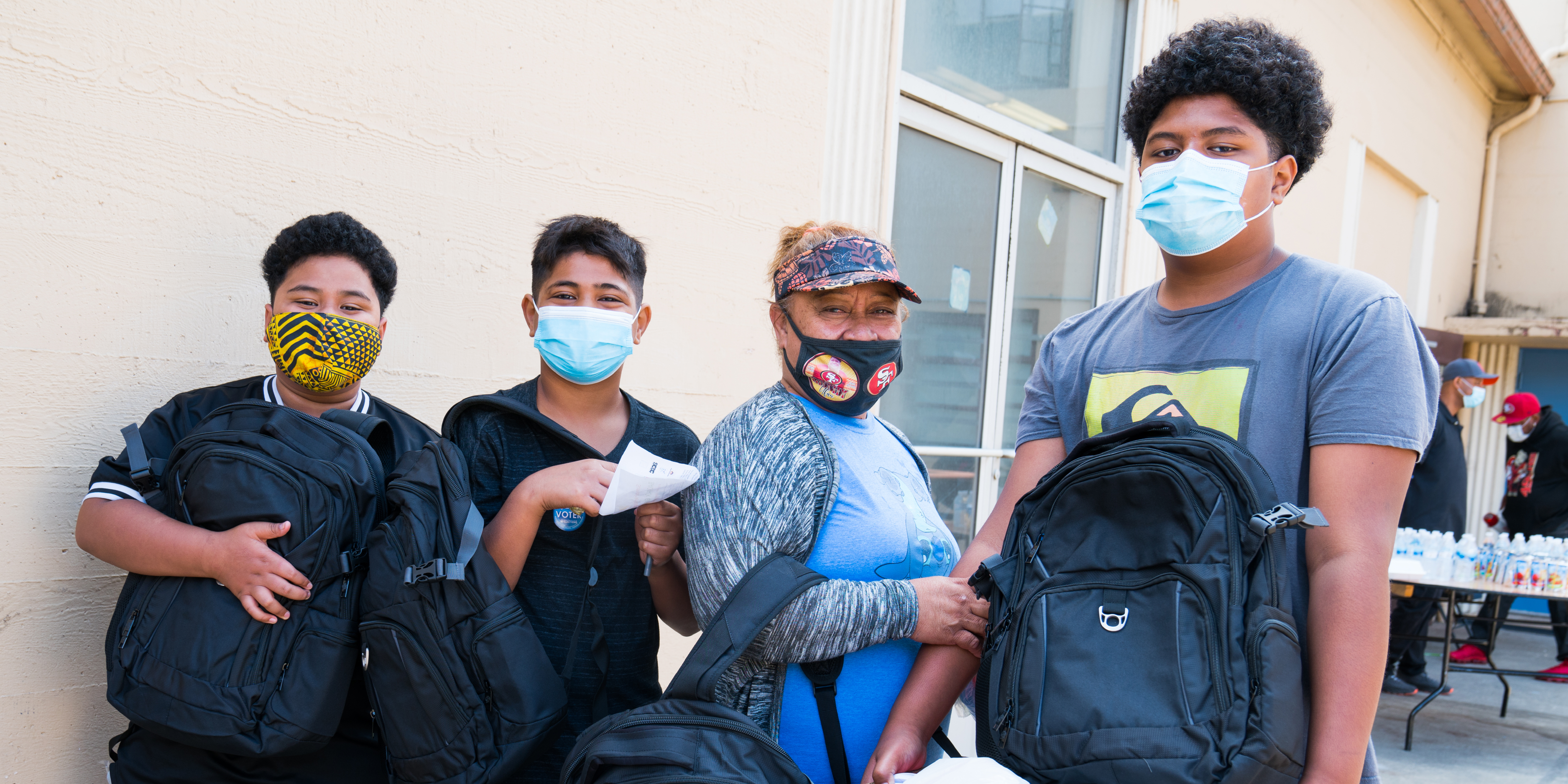 Mercy Housing Residents are smiling towards the camera holding backpacks filled with back to school goodies